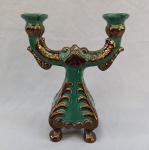 FAIANÇA, um (1) candelabro para dois lumes, modelagem relevada em elementos vegetalistas e volutas, pés com terminações em garra, tonalidade verde com detalhes em ouro velho, sem marca de manufatura aparente, medindo 22,5 cm altura.