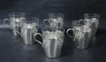 METAL - Seis porta copos em metal espessurado à prata com decoração de caneluras e arabescos , bordas serrilhadas e alças vazadas. Acompanha 6 copos em vidro translúcido. Medida 8 cm X 10 cm.