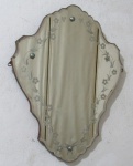 ESPELHO, um (1) em cristal veneziano na forma de escuso, borda recortada e bisotada, ornamentação em torno com guirlanda floral, suporte em madeira com pinos de fixação com acabamento convexo, faltando um deles, medindo 63 x 48 cm, usado.