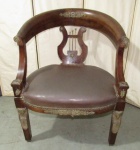 MOBILIÁRIO, uma (1) antiga poltrona, padrão Império, estrutura entalhada  em madeira, com apliques diversos em bronze, tipo gondola, braços curvilíneos continuação do cachaço, tabela na forma de lira, assento com forração em courvin preso com tacheados, medindo 83 x 62,5 x 48 cm, sinais de uso e pequenos defeitos, vide fotos extra.