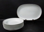 PORCELANA REAL S. PAULO - Sete pratos fundos e uma travessa ovalada, em porcelana nacional vitrificada branca, bordas trabalhadas com frisos sutilmente relevados e adornadas com generoso filete em pintura à ouro, marcados no fundo. Med. pratos: 23 cm de diâmetro/ travessa: 37 cm de comprimento x 24,5 cm de largura.