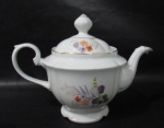 PORCELANA REAL S. PAULO - Elegante bule para chá em porcelana vitrificada branca, delicadamente decorado com motivos vegetalistas em exuberante policromia, bordas movimentadas e filetadas à ouro, pega da tampa em forma estilizada de flor, alça vazada finalizando em voluta, marcado no fundo. Medidas: alt total 18 cm x larg total 26 cm.