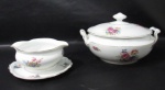 PORCELANA SHCMIDT - Uma sopeira e uma molheira com presentoir em porcelana nacional com esmaltagem branca, decoradas com elementos vegetalistas em rica policromia, bordas onduladas e filetadas à ouro, marcadas no fundo. Med. maior: alt total 15 cm x larg total 26,5 cm/ menor: alt total 8 cm x larg total 17 cm. Tampa da sopeira com bicados na borda, e molheira com bicado na borda do presentoir.