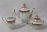 PORCELANA - REAL S. PAULO - Um bule para café, um açucareiro e uma cremeira em porcelana vitrificada branca com efeito perolizado, bordas onduladas e adornadas com largas faixas na cor vinho, sobrepostas com guirlandas de flores, folhas e filetes em pintura à ouro, pegas das tampas em forma de pinha, alças e bico com vasta douração, marcados no fundo. Medidas: maior: alt total 18 cm x larg total 18,5 cm/ menor: alt 10 cm x larg total 11 cm. Açucareiro com fio de cabelo em uma na alça.