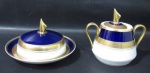 PORCELANA - STEATITA PARANÁ - Elegantes açucareiro e manteigueira em porcelana vitrificada branca, com bordas adornadas com largas faixas sendo na tonalidade azul cobalto, e gravação legitima, generoso filete e friso em pintura à ouro, pegas das tampas estilizadas e alças vazadas com vasta douração, marcados no fundo. Med. açucareiro: alt total 11 cm x larg total 13,5 cm/ manteigueira: alt total 8 cm x diam total 15,5 cm.