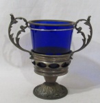 VIDRO / METAL DOURADO - Antigo balde para gelo em vidro na cor azul marinho, guarnecido com metal dourado na borda, apoiado sobre base no mesmo metal, com bojo ornado com figuras ovaladas vazadas, alças trabalhadas em folhas e volutas, finalizando com pé bolacha ricamente cinzelado. Med. totais: alt 21,5 cm diam da borda 12,5 cm x larg total 22 cm. Metal apresenta marcas do tempo.