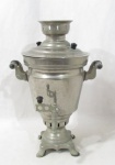 METAL PRATEADO - Um (1) Samovar russo decorativo em metal prateado, apoiado sobre base quadrada e pés em garras, com alça fixa. Marcação no metal no centro, Altura 40 cm.