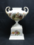 PORCELANA EUROPEIA - Antiga ânfora sobre base quadrada em tonalidade branca, decorada com flores policromadas e cena central galante e detalhes dourados. Med. 25x19x11 cm.