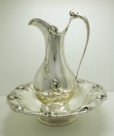 PEWTER - Magnífico gomil (jarro com bacia) em pewter espessurado a prata, decoração em relevo floral. Apresenta amassados nas bases. Med. jarro Alt. 49 cm e bacia 12x48 cm.