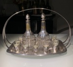 METAL PRATEADO  ANTIGA LICOREIRA EM METAL PRATEADO, CONTENDO 2GARRAFAS E 6 COPOS PARA LICOR DESGASTES E MARCAS DE USO. FALTA VIDRO EM UMA DASTAMPAS DA GARRAFA, OUTRA TAMPA DA GARRAFA COM PONTA DO VIDRO QUEBRADA EMETAL CRAQUELADO E DESGASTADO. PÉS EM BOLA. MEDIDA TOTAL DA LICOREIRA: 38,5X25.
