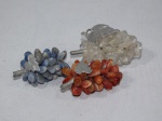 Três cachos de uva confeccionados em pedras polidas sendo um translúcido, um azul e um vermelho. Medida do maior 8 cm.