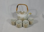Bule para chá e 4 copinhos em porcelana branca decorada com bambuzal em tom de marrom, alça em madeira e palhinha. Alça quebrada. Med. do bule 14cm.