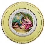 NADIR - Elegante prato para coleção em porcelana esmaltada ricamente adornada com cena galante ao centro e contorno em vibrante ouro. Assinado no canto inferior. Possui registro da manufatura na base. Mede 21cm de diâmetro.