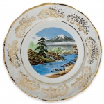 Elegante prato para coleção em porcelana branca esmaltada ricamente adornado com paisagem ao centro em policromia e contorno em vibrante ouro. Possui registro da manufatura na base. Mede 24cm.