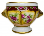 Elegante floreira em porcelana branca esmaltada ricamente adornada com motivo floral em policromia e contorno em vibrante ouro pintada a mão, com alças em formato de cabeça de leão. Assinada no canto inferior. Mede 14cm de altura x 22cm de comprimento.