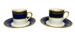 SIMPSONS ENGLAND - Par de elegantes xícaras para café em requintada porcelana inglesa esmaltada na cor azul royal, ricamente adornada com ramos gregos de louro em vibrante ouro. Acompanham seus respectivos pires. Possui registro da manufatura SIMPSONS POTTER'S COBRIDGE ENGLAND na base.