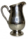 Antiga jarra com estrutura em metal espessurado a prata com alça adornada com arabescos. Marcas do tempo. Mede 22cm.