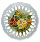 Gracioso prato para parede em porcelana branca esmaltada, ricamente adornado com motivo floral em policromia pintado a mão e borda vazada. Assinada no canto inferior e datado. Mede 20cm.