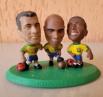 Mini craques da Coca Cola, copa de 98. Na peça estão os jogadores, Ronaldo, Dunga e Romário, encima de uma plataforma verde. Está significativamente danificado, com desgastes na base e cabeça dos jogadores. Altura: 7,5cm; Comprimento: 11,5; Largura: 6,5cm.