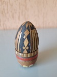 Antigo ovo de madeira decorado, com padrões geométricos em madeira. Possui uma base com desenhos pintados ao seu redor. Infelizmente tem origem indeterminada. Altura: 8cm; Diâmetro: 4cm.
