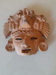 Antiga escultura de máscara em cerâmica, de provável origem zapoteca ou inspirada nessa civilização, representando um sacerdote. A peça possui marcas do tempo na boca. Altura: 15cm; Comprimento: 15cm.