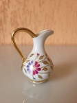 Antiga jarra em miniatura, feita no Japão, em porcelana ST. Com alça e detalhes, decorada em folha de ouro, a peça tem flores pintadas em seu entorno. Altura: 7cm; Largura: 5,5cm.