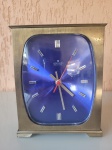 Antigo relógio de mesa, da marca Junghans Eletronic. Possui caixa de metal amarelo e é movido à pilha. A peça é dos anos 70/80 e tem o mostrador azul cobalto de aspecto metálico. Altura: 16cm; Comprimento: 13cm; Largura: 5cm.