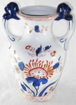 Ânfora em porcelana branca pintada a mão com folhagens e flores em azul e rouge-de-fer. Assinado na base. Med.: 22,5x17cm.