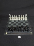 Tabuleiro de xadrez em Vidro com 32 peças. 2 peças apresentam bicados Medida: 25 cm x 25 cm