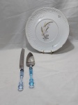 Prato de bolo em porcelana com faca e espátula em aço inox com pega em acrílico. Medindo o prato 28cm de diâmetro.