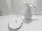 Lote composto de jarra e travessa oval rasa em porcelana. Medindo a jarra 29,5cm de altura x 21cm bico alça. Jarra com fio de cabelo.