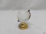 Enfeite na forma de globo terrestre com base em metal dourado e globo em vidro. Medindo 9cm de altura.