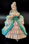 Figura de dama aristocratica em biscuit. Usando esvoaçantes vestes em tons de rosa e azul esverdeado, sentada a cadeira. Medindo 16,5cm de altura por 13,5cm de comprimento.
