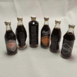 COLECIONISMO - Lote com 06 (seis) mini garrafas Históricas de COCA-COLA, todas lacradas e com líquido no interior. Cada uma mede aprox. 7,5 cm de altura. Garrafas Históricas da Coca-Cola dos anos de 1899 - 1900 - 1905 - 1913 - 1915 - 1923.