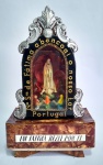 Portugal - Antigo e belo Oratório, Luminária e Musical à corda - Representando Nossa Senhora de Fátima - ''Em Fátima Rezei por Ti'' - Estrutura em madeira, frente em vidro com Apliques em metal prateado - Caixa musical funcionando - Obs: A luminária necessita de tomada e revisão, e possui algumas partes das folhas em galalite que estão descolando - Conforme fotos - Medida: 24 x 14 x 7,5 cm.