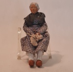 Bibelô de porcelana, com corpo e vestimenta em tecido, representado senhora sentada  -  Medidas aproximadas  20 cm de altura