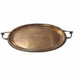 Grandiosa bandeja de servir, em metal espessurado a prata, bordas toda ornamentada em relevos ao feitio de esferas, ao centro decorado no padrão arabescos. Medida: 68cm x 40cm.
