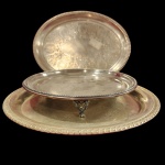 Lote conjunto, composto por três pecas, espessurado a prata, sendo duas travessas de servir e um centro de mesa com pés em formato de cabeça de leão. Medida menor: 25cm x 5cm. Maior: 32cm.