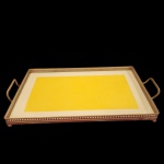 Grande Bandeja de servir, estilo art deco, com fundo em fainça no tom amarelo e branco, com laterais em metal decorado em galeria vazada, encimado por pés em formato de esferas. Medida: 25cm x 44cm. Obs um pé em esferas faltando.