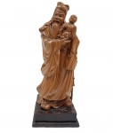 Magnifica estatueta "Shou Xing", representando figura sábia segurando uma criança, com finos detalhes meticulosos em suas vestes e expressões, com base em madeira no tom preto. Estatueta identificada como uma divindade ou figura de sabedoria que carrega uma criança, simbolizando proteção, fertilidade e continuidade familiar. Medida: 30cm x 12cm.