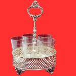 SANT LUIS - Conjunto contendo cinco copos, em cristal sant Luis, art deco anos 50, com rica lapidação, no padrão arabescos em relevo. Acompanha elegante suporte em metal prateado no estilo art nouveau anos 50, ricamente decorado em galeria vazada. Medida total: 30cm x 25cm x 20cm.