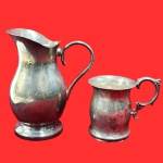 Conjunto contendo duas pecas antigas, sendo uma leiteira e um copo com alça ornamentada, em metal prateado. Medida: 18cm x 16cm.