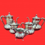 Antigo conjunto de chá e café, estilo clássico do início do século XX, com ricos detalhes em caneluras e alças ornamentada. Peças em metal prateado, contendo cinco peças, sendo dois bules, duas leiteira, uma açucareiro, de diferentes marcas.