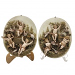 PORCELANA - Conjunto contendo par de placas ovais de porcelana vintage anos 50, retratando querubins em um cenário de jardim, com ricos detalhes de folhagens e anjos em relevos . Medida: 30cm x 22cm. Obs: no estado.