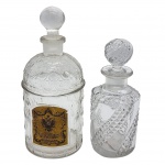 Par de perfumeiros antigos, composto por um frasco em cristal francês Baccarat e outro frasco de perfume vintage da renomada marca Guerlain. Datados do século XIX, apresentam um refinado estilo de lapidação conhecido como Serpentine ou bico de jaca, caracterizado por faixas onduladas que conferem movimento e sofisticação às peças. Medida: 20 cm de altura e o menor 18 cm. Observação: uma das tampas encontra-se travada.