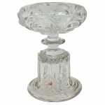 BACCARAT - Antiga compoteira em cristal da tradicional marca francesa Baccarat, em formato de taça rasa com bordas levemente onduladas. A peça apresenta padrões decorativos de corpo cilíndrico robusto, adornado por frisos verticais, e repousa sobre uma base circular plana que confere estabilidade e um aspecto clássico. Medidas: 17 cm x 13 cm.
