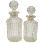 Par de perfumeiros vintage, com corpo bojudo em caneluras e formato quadrado adornado por relevo geométrico. Cada peça possui rolha esférica facetada, trabalhada no padrão de diamante, que acrescenta brilho e sofisticação ao conjunto. Medida: 19 cm e o menor 16 cm. Observação: uma das tampas encontra-se travada.