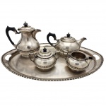 Broqua & Scholberg  Jogo de chá e café antigo em estilo Art Déco, datado da década de 1950. O conjunto é formado por um bule de café alto, um bule de chá mais baixo e arredondado, um açucareiro com tampa e uma cremeira sem tampa. Os bules possuem alças curvas escuras, em  baquelite, com pomos superiores combinando nas tampas. Todas as peças apresentam design clássico, com frisos canelados ao longo das bordas e bases, além de uma pátina natural do tempo. Acompanha bandeja de servir.