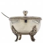 Tigela de sobremesa com tampa e colher, em metal prateado de alta qualidade (espessura prata 90). Corpo hemisférico liso e polido, sustentado por três pés ornamentados em estilo rococó. Borda com friso perolado e tampa com pomo esférico em gomos. Apresenta pátina natural e leves marcas de uso, preservando o brilho da prataria fina. Medida: 9cm.