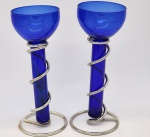 Par de candelabros para uma vela, em vidro no tom azulcobalto, com suporte em metal espessurado a prata. Medida: 26 cm.